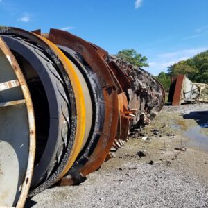 Rusty industrial pipe lying on gravel ground.