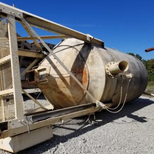 Rusty industrial tank lying on gravel ground.