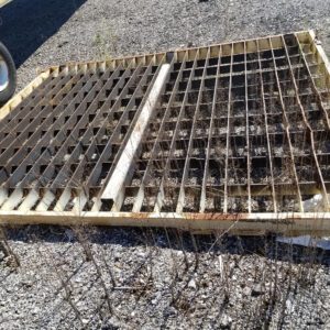 Metal grate lying on gravel ground.