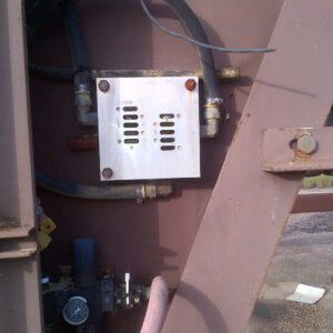 Metal box attached to industrial machinery outdoors.