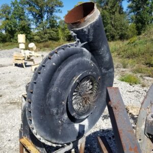 Rusty industrial fan outdoors on gravel.