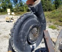 Rusty industrial fan outdoors on gravel.