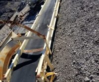 Conveyor belt on rocky terrain under sky.