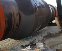 Large rusty metal pipe on gravel ground.